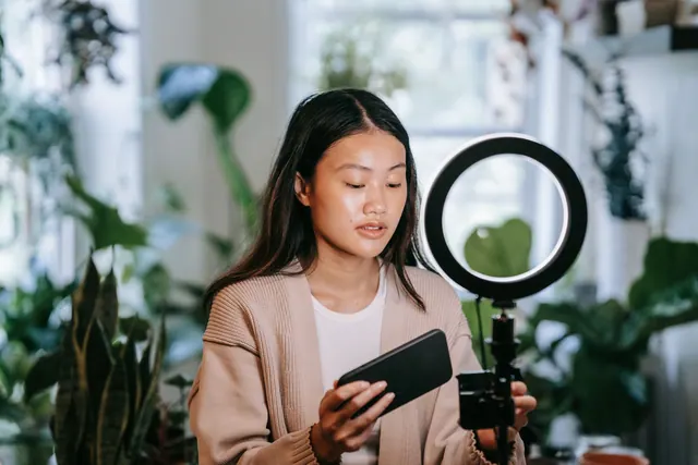 Asian woman adjusting smartphone and ring light indoors for video recording. Best strategy and objectives agencies 2027: guide