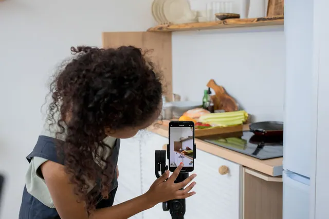A woman with curly hair films a cooking video using a smartphone stabilizer in a modern kitchen. How to approach best strategy and objectives tools in practice