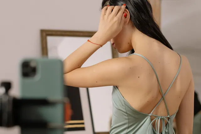 Woman in strappy dress styling hair while filming with smartphone indoors. Why a suitability standard should exist before a fraud case forces one